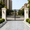 Elegant black wrought iron gate with marble pillars in a residential area.